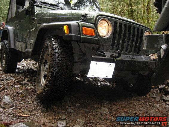 Front right view of a dark green Jeep Wrangler on a muddy forest trail.