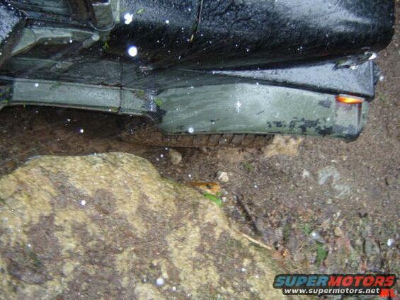 Rear fender and tire of a dark vehicle next to a large rock.
