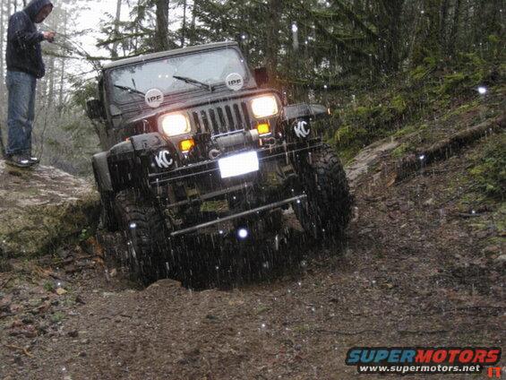Jeep Wrangler off-roading on a muddy trail in the rain.