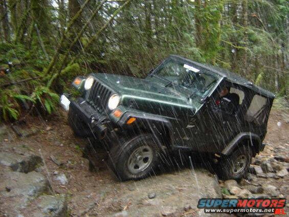 Dark green Jeep Wrangler off-roading on a rocky, wet trail in a forest.