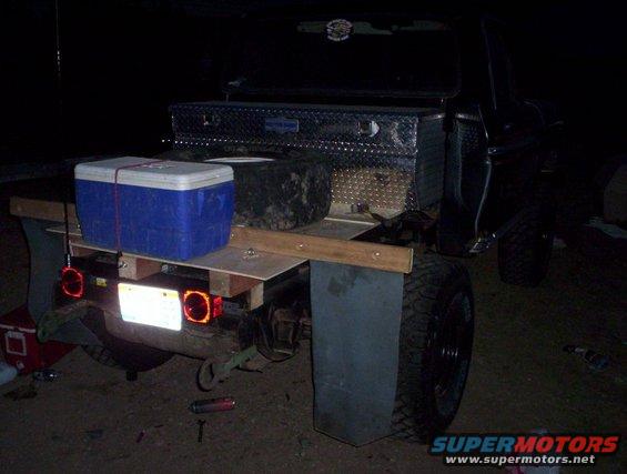 Truck bed with blue cooler, toolbox, and spare tire. Rear view