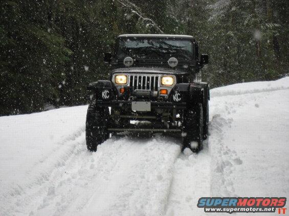 Black Jeep Wrangler driving in snow with trees in background