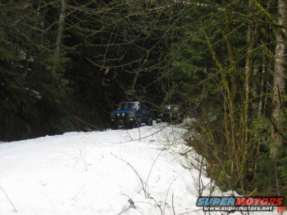 Blue 1980s Ford Bronco on a snowy forest road.