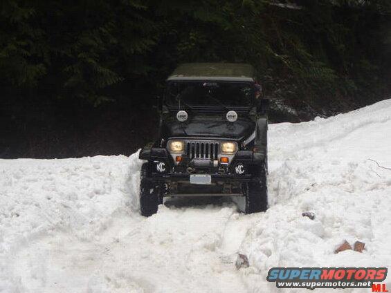 Black Jeep Wrangler driving through snow with KC lights.