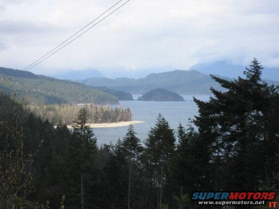 Cloudy day over a body of water with forested hills and mountains.
