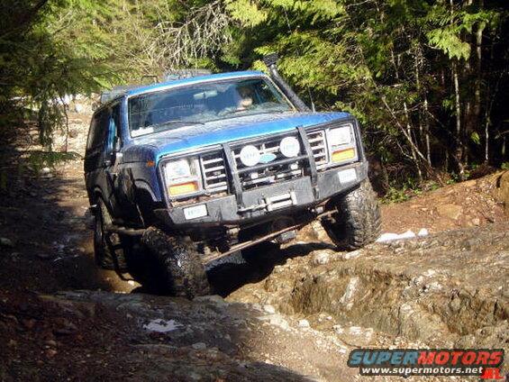 Blue first-gen Ford Bronco off-roading on a rocky trail.
