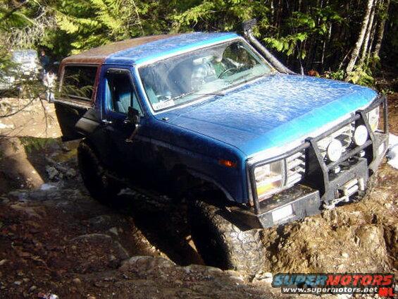 Blue 1985 Ford Bronco off-roading on a muddy trail.