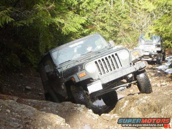 Black Jeep Wrangler tilted on a rocky, muddy trail with another Jeep behind it.