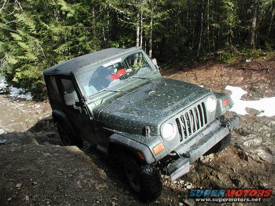 Dark green Jeep Wrangler off-roading on a rocky, muddy trail.