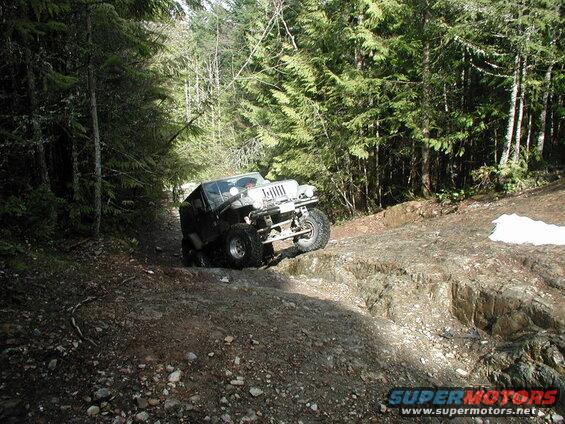 Modified Jeep Wrangler climbing a rocky, wooded trail.