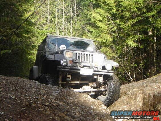 Black Jeep Wrangler off-roading on a rocky trail in a forest.