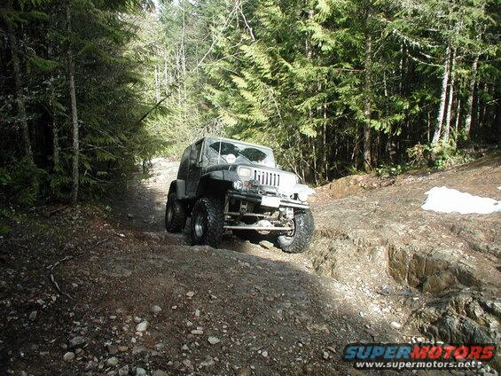 Modified Jeep Wrangler driving on a rocky, wooded trail.