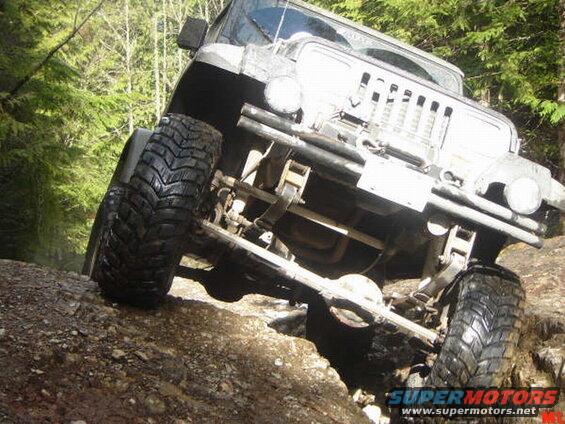 Off-road vehicle with large tires climbing a rocky hill in a forest.
