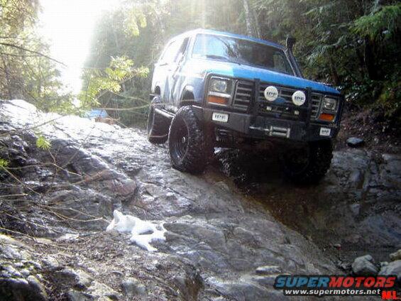 Blue 1985 Ford Bronco off-roading on a rocky trail