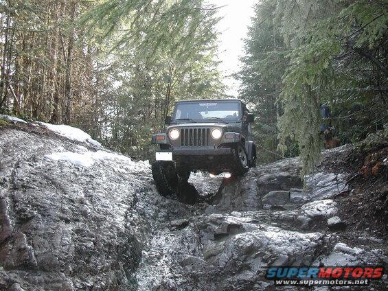 Green Jeep Wrangler driving on a rocky, snowy off-road trail.