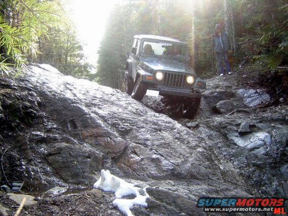 Jeep Wrangler climbing a rocky off-road trail with sun flare.