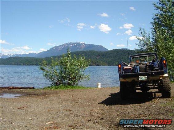 Blue Ford pickup truck parked by a lake with mountains in the background.