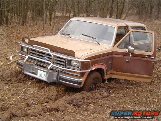 Brown and tan Ford Bronco stuck in mud, driver's door open
