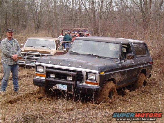Black 1978 Ford Bronco stuck in mud with a man standing nearby