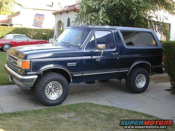 Dark blue Ford Bronco parked in a driveway. Red convertible parked in background