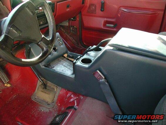 Interior of a red 1990 Ford F-250 showing the center console, steering wheel, and gear shifter.
