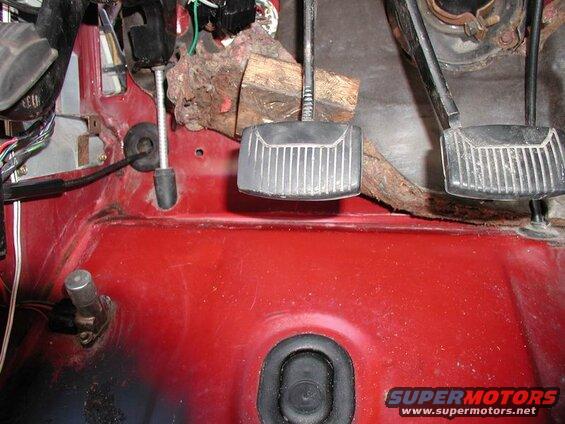 Interior of a red vehicle showing clutch and brake pedals, wires, and a grommet.