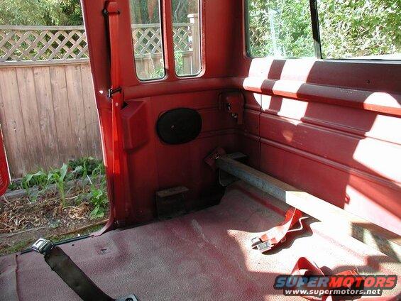 Interior of a red 1990 Ford F-250 pickup truck, showing the rear bench seat, seatbelts, and a metal bar.
