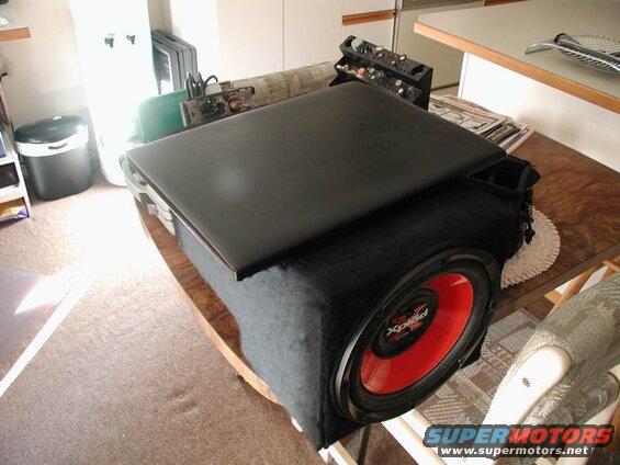 Black subwoofer with red speaker and open black laptop on a table.