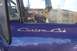 1959 Ford F-100 - The 'Custom Cab' emblem is visible on the side of a purple truck, with a reflection in the window.