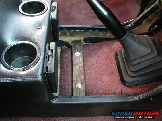 Interior of a vehicle showing a black center console with cup holders and a wooden support block near the gear shifter.