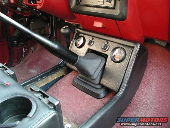 Vehicle interior showing gear shifter, voltage gauge, and red dashboard trim.