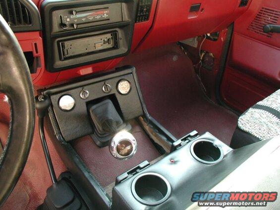Interior of a vehicle with custom center console, gear shifter, cupholders, gauges, and aftermarket stereo.