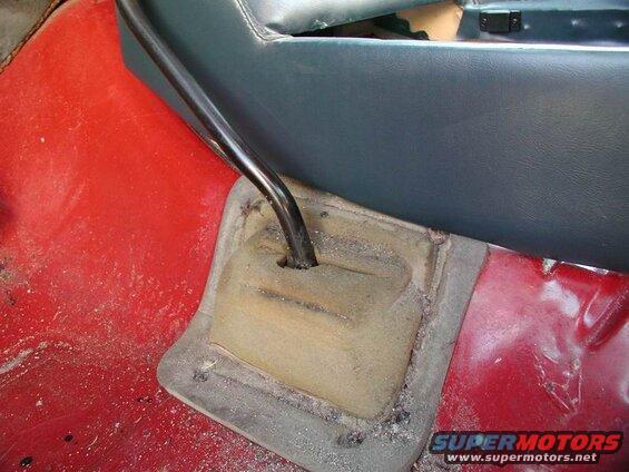 Close-up of gear shift lever and boot on red floor inside a vehicle.