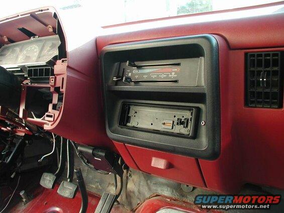 Interior view of a red dashboard with a disassembled radio bezel and exposed wiring.