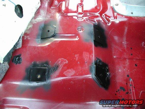 Red vehicle interior floor with black patches and bolt holes.
