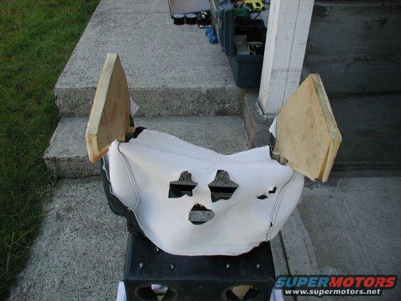 White material with cutouts resembling a face, propped up by wooden pieces.