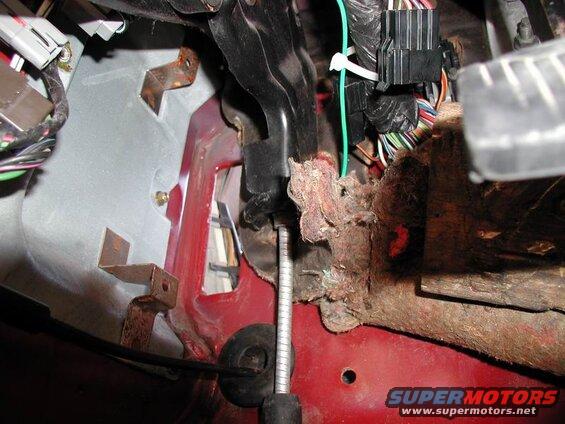 Close-up of vehicle's driver side footwell with brake pedal, wiring, and firewall.