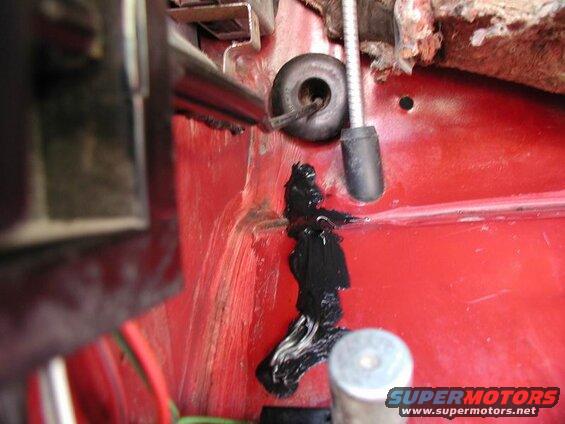 Black sealant applied over wires on a red surface with a rubber grommet.