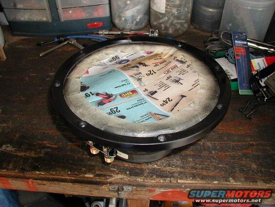 Car speaker with newspaper lining on a workbench with tools.