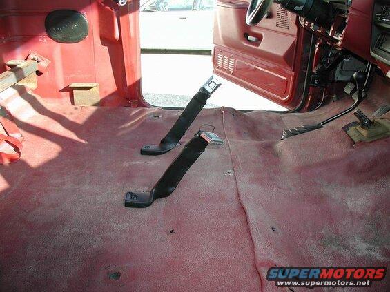 Interior of a red Ford F-250 pickup truck showing the floor and two seatbelts.