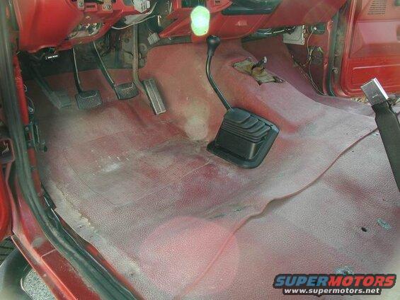 Interior of a red pickup truck showing pedals, manual shifter, and red carpet.