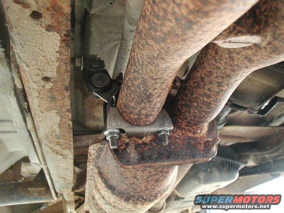 Close-up of a catalytic converter clamp on a rusted exhaust system of a vehicle.
