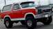 1985 Ford Bronco - This red and white Ford Bronco is parked outdoors, showing its front three-quarter view.