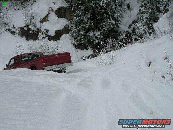 Red Ford F-250 stuck in deep snow on a wooded hillside.