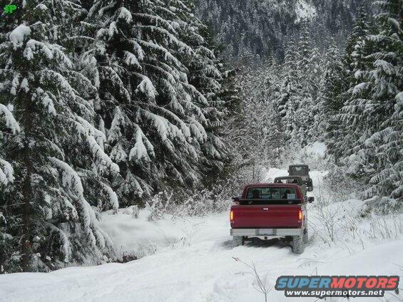 Red Ford F-250 driving on a snowy forest road with other vehicles.