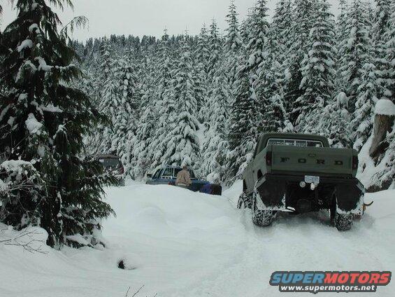 Green Ford F-250 pickup truck in deep snow with snow-covered trees.