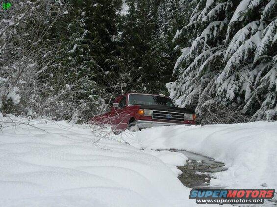Red Ford pickup truck stuck in a snowy creek.