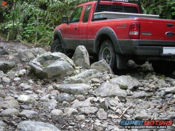 Red Ford pickup truck driving on a rocky trail.