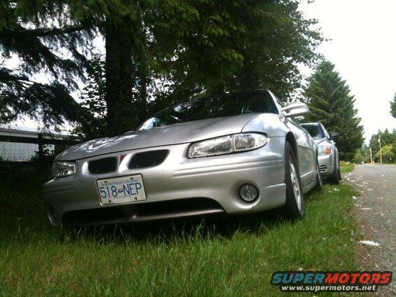 Silver Pontiac Grand Prix parked on grass next to a road.
