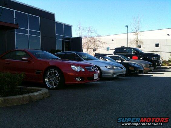 Red coupe, silver sedan, black coupe, and black pickup truck parked in a lot.